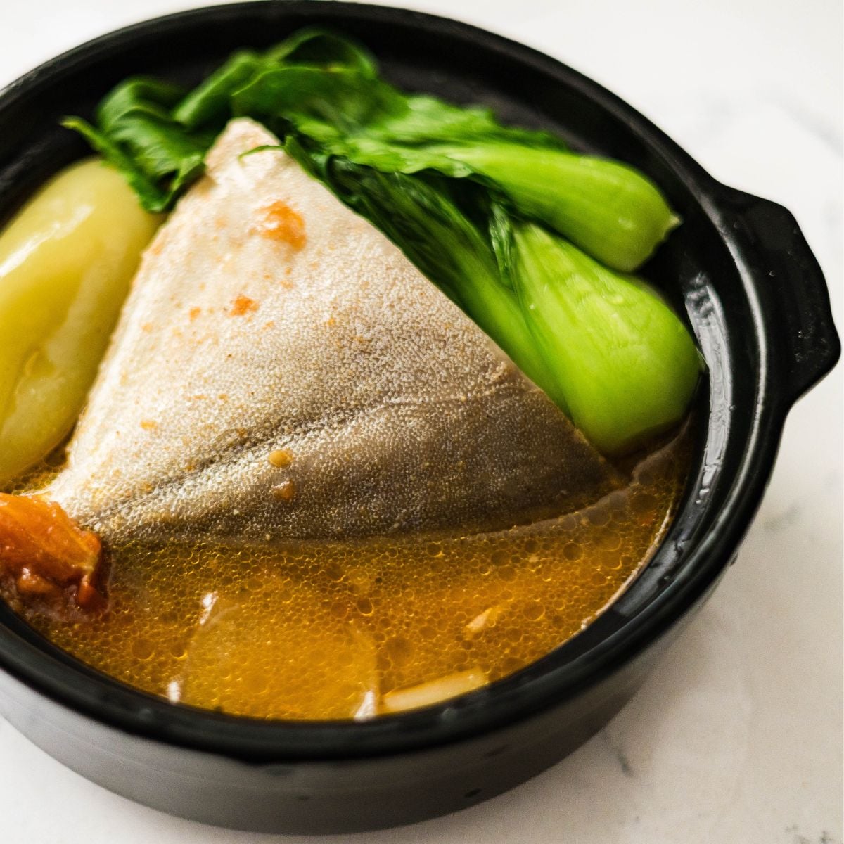 A bowl of sinigang sa miso with pompano, bok choy, tomatoes, and warm sour broth.