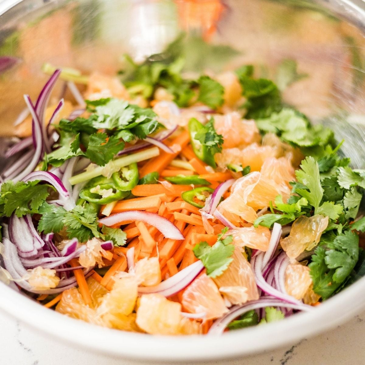 Close-up of pomelo salad with cucumber, carrots, red onion, cilantro, chili, and chopped peanuts.