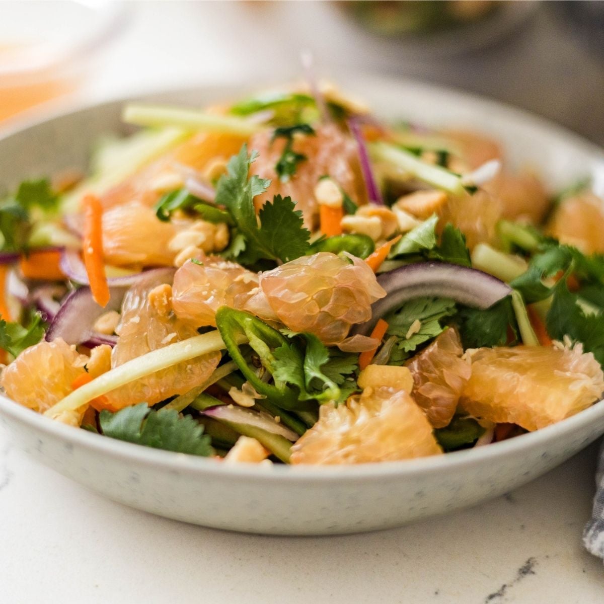 Fresh pomelo salad ingredients in a mixing bowl with carrots, red onion, cucumber, chili, and cilantro