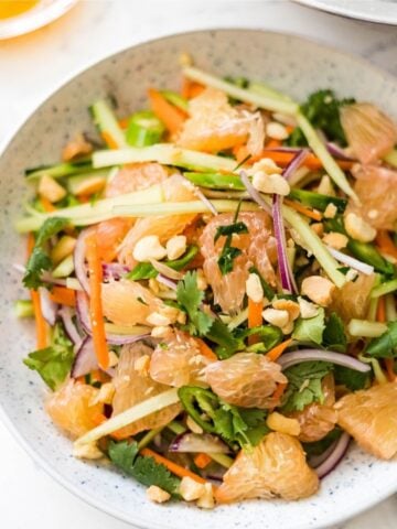Pomelo salad with cucumber, carrots, red onion, cilantro, chili, peanuts, and fresh herbs in a bowl.