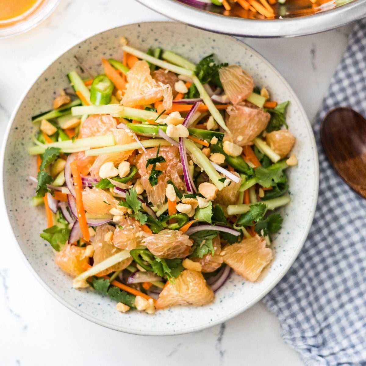 Pomelo salad with cucumber, carrots, red onion, cilantro, chili, peanuts, and fresh herbs in a bowl.