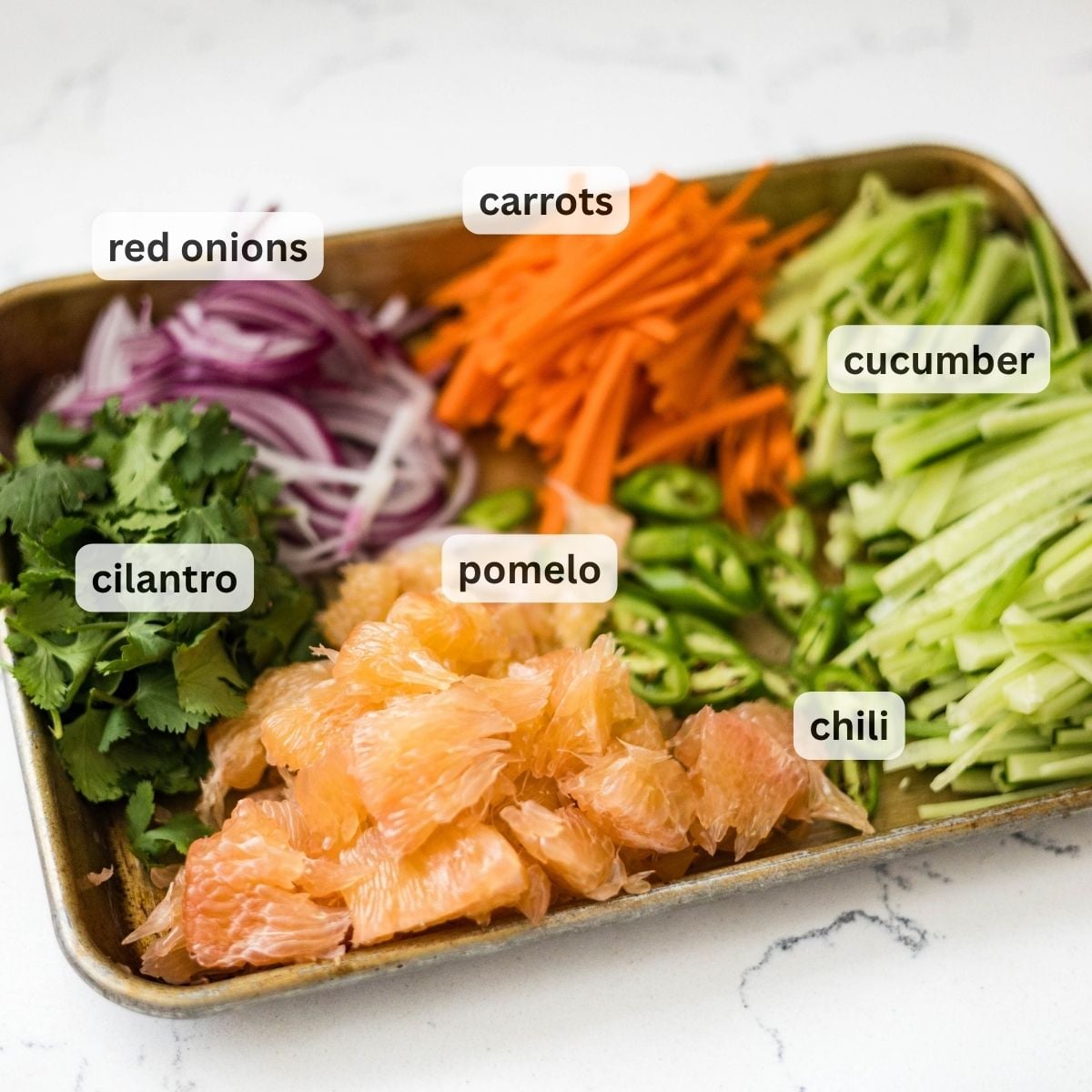 Tray of prepped pomelo salad ingredients labeled red onions, carrots, cucumber, cilantro, pomelo, and chili.