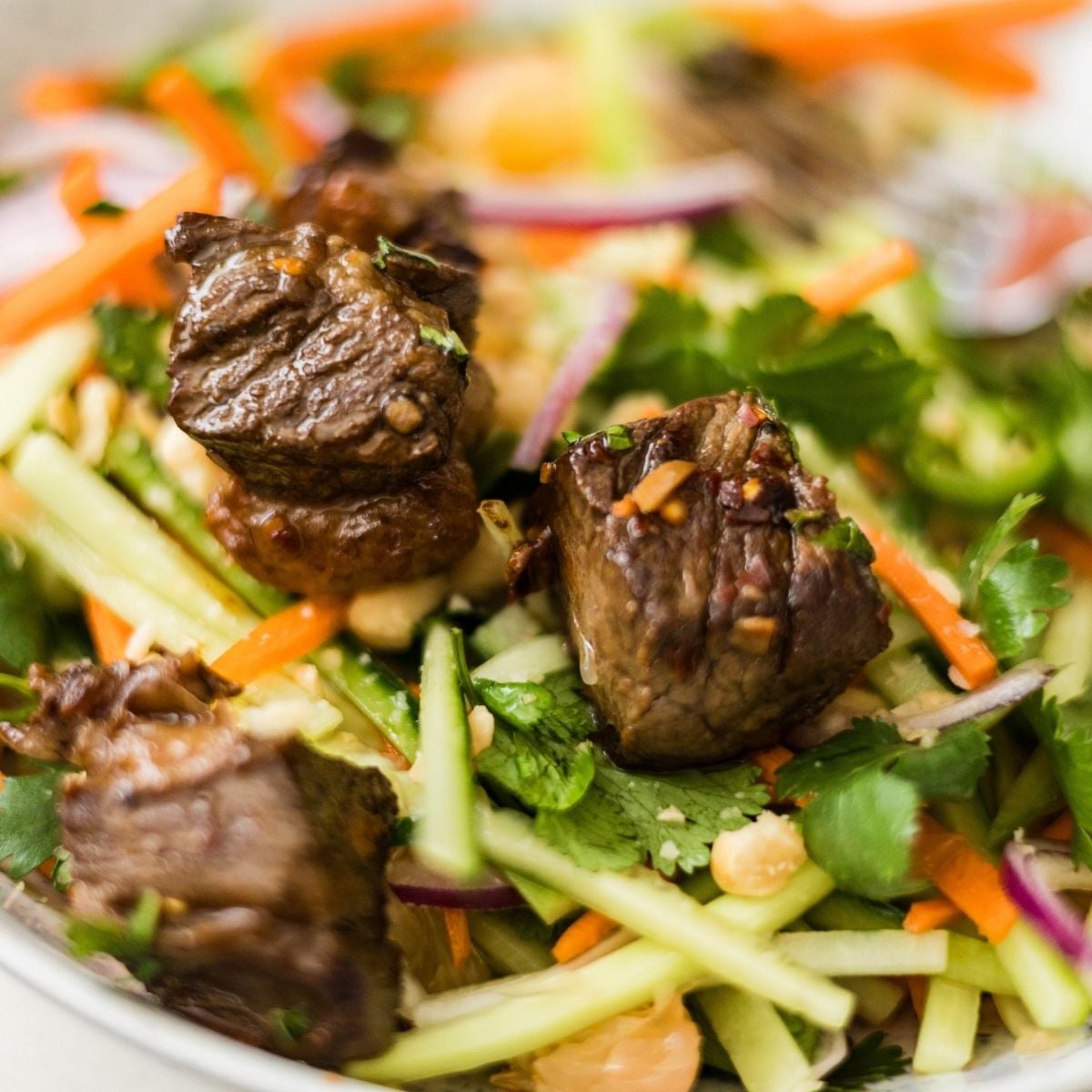 Seared beef pieces served over pomelo salad with cucumber, carrots, red onion, cilantro, chili, and peanuts.