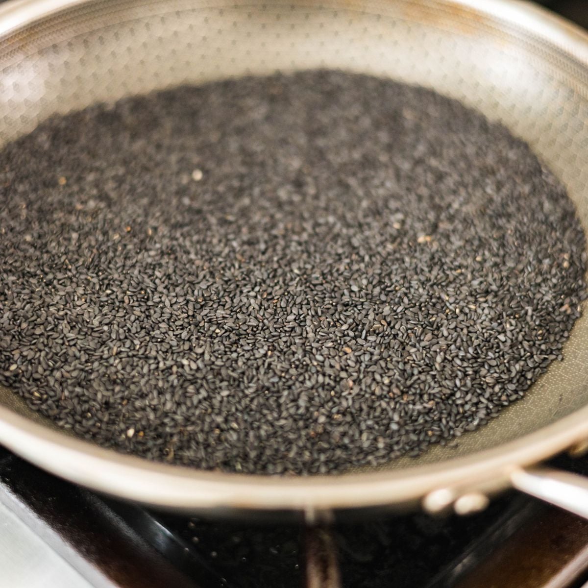 Black sesame seeds toasting in a skillet before blending into paste