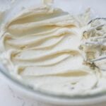 Creamy vanilla buttercream frosting whipped smooth in a glass bowl with mixer beaters.