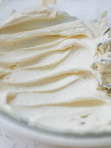 Creamy vanilla buttercream frosting whipped smooth in a glass bowl with mixer beaters.
