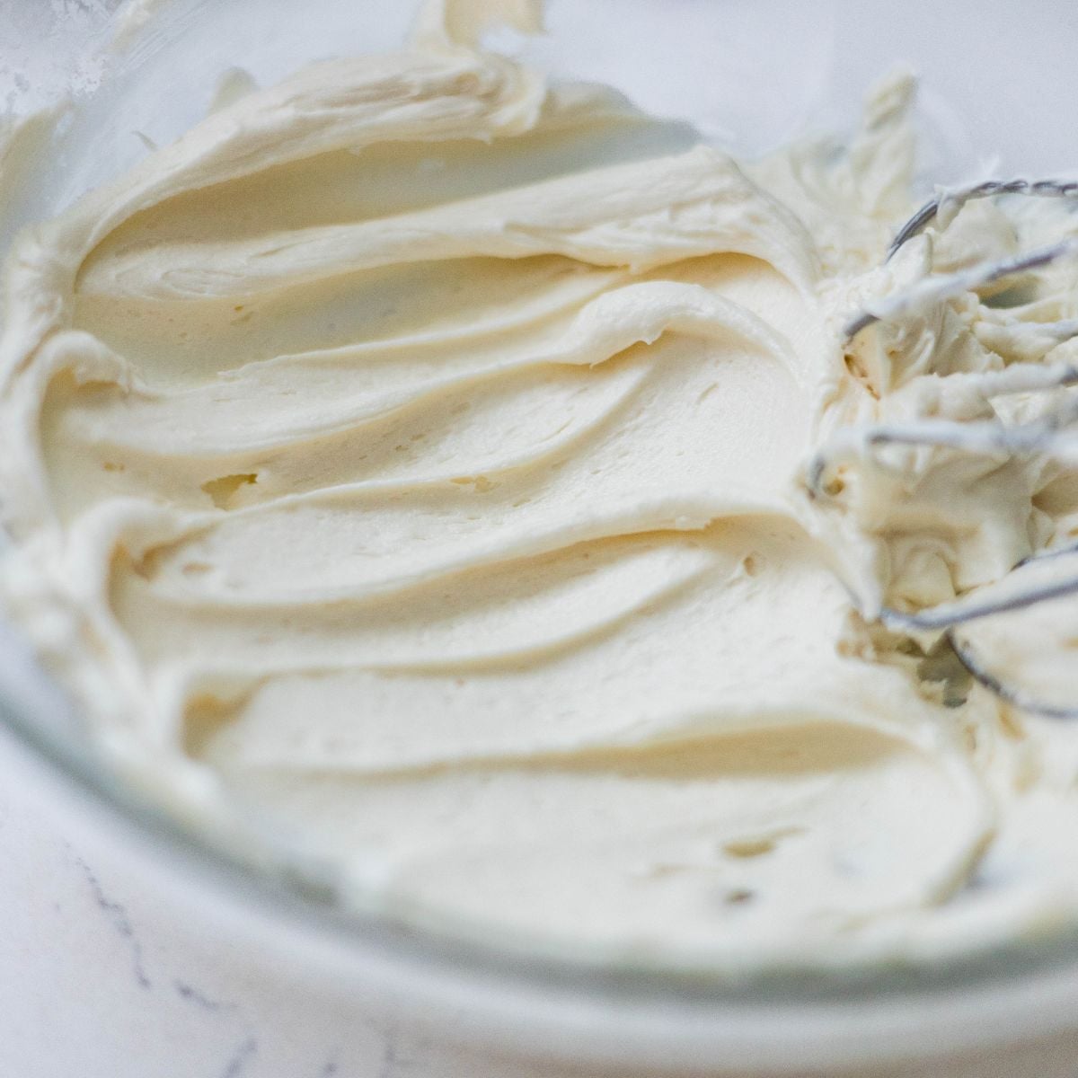 Creamy vanilla buttercream frosting whipped smooth in a glass bowl with mixer beaters.