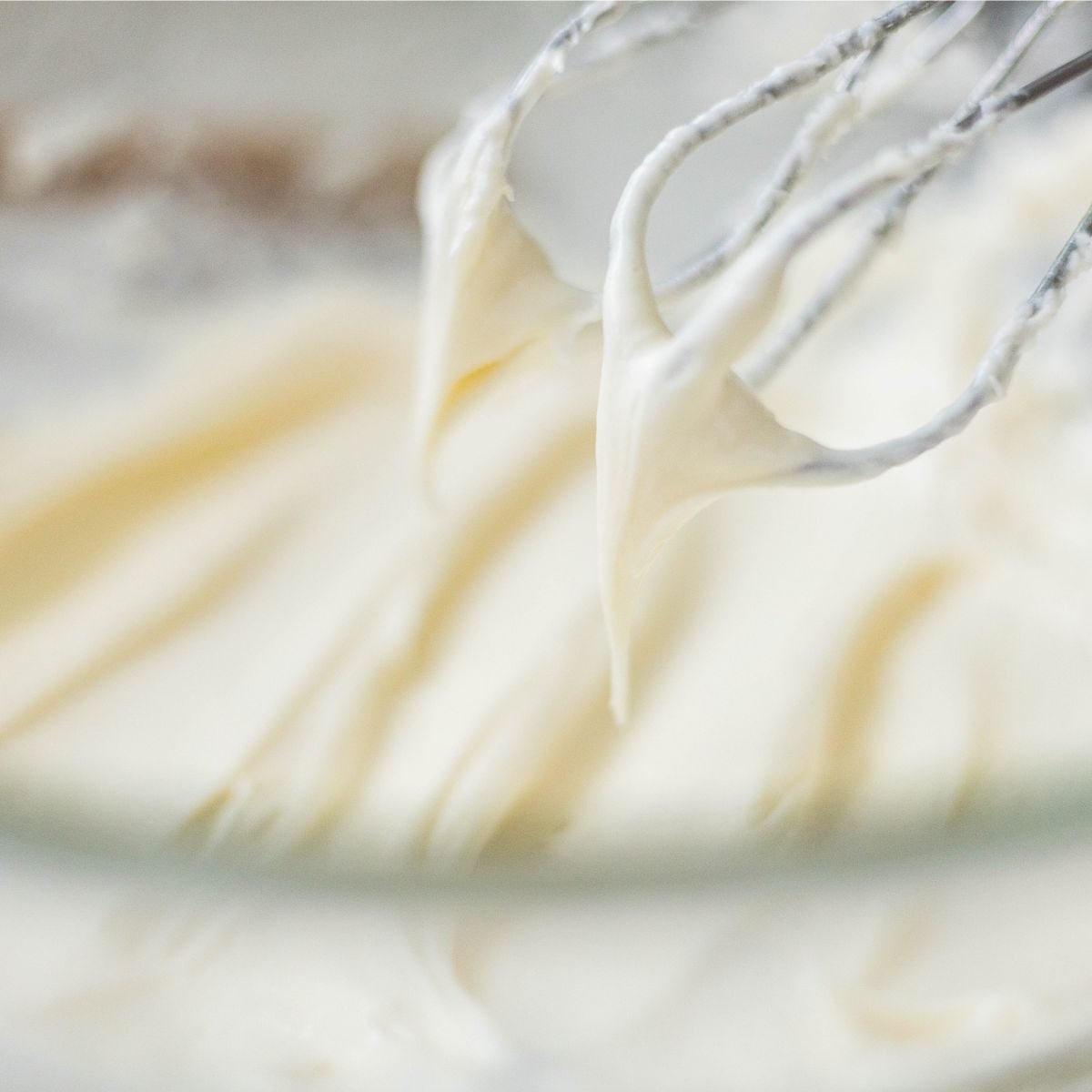 Whisk attachment lifting soft peaks of smooth vanilla buttercream frosting from a bowl.