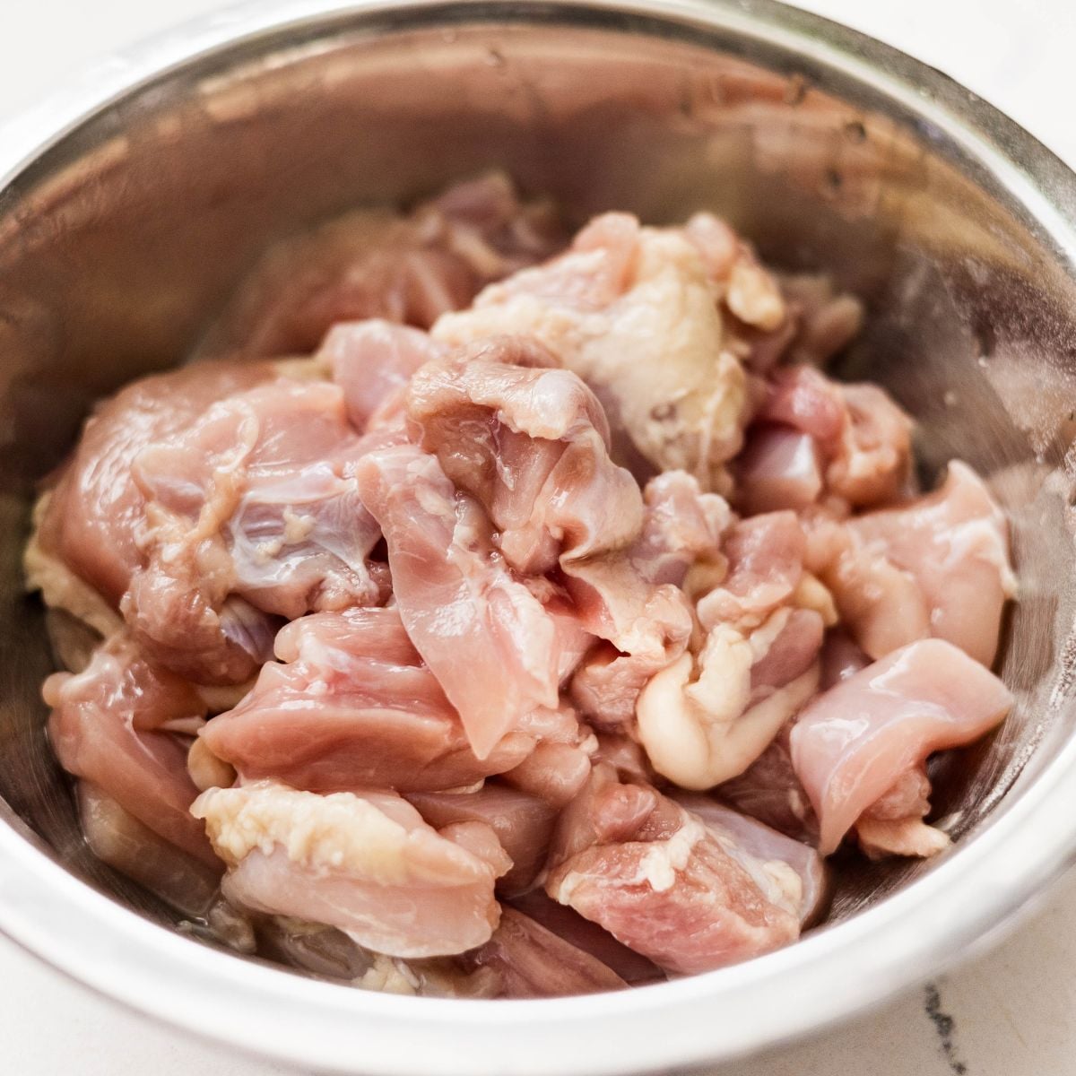 Chopped raw chicken thighs in a stainless steel bowl before marinating.