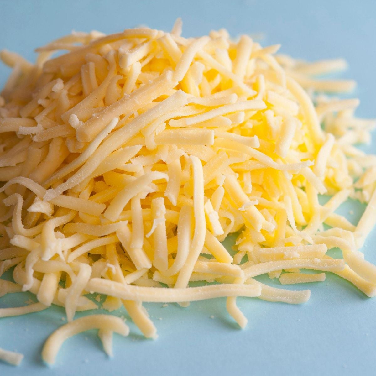 Pile of freshly shredded cheese on a light blue surface.