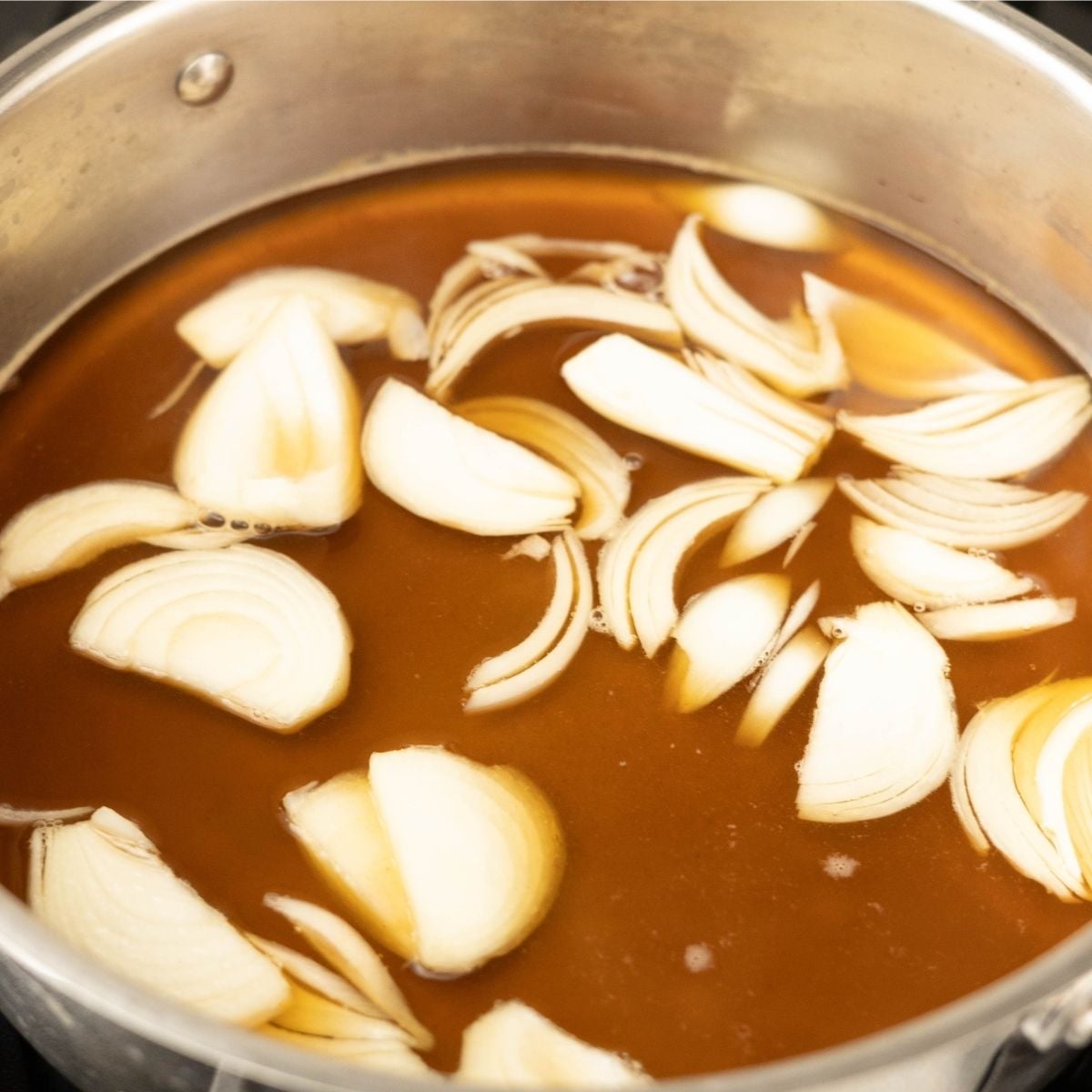 Sliced yellow onions in dashi broth in a shallow pan