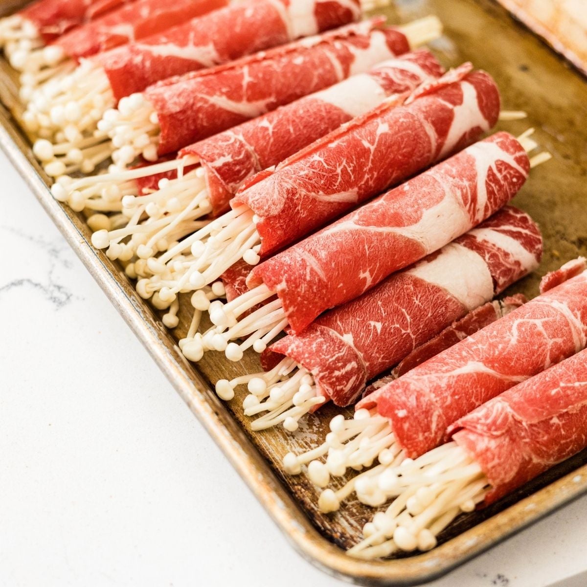 Frozen beef chuck rolls filled with thin bundles of enoki mushrooms before cooking