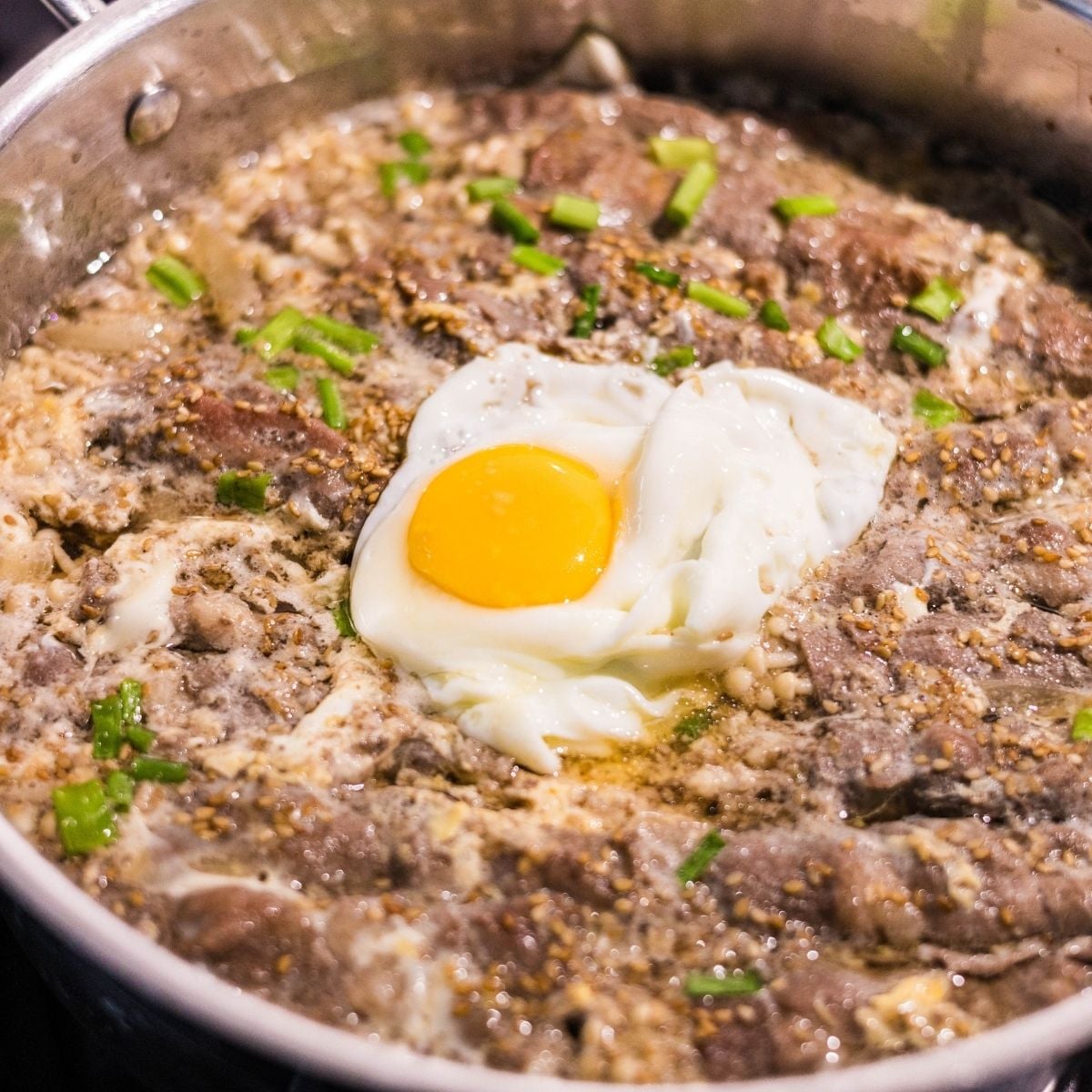 Finished enoki beef rolls topped with a soft egg and green onions, served in the pan