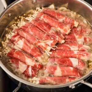 Enoki beef rolls simmering in dashi broth until the beef loses its pink color
