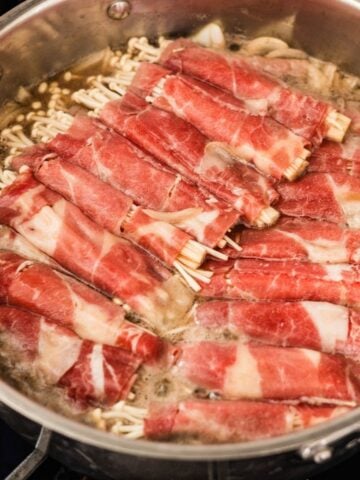 Enoki beef rolls simmering in dashi broth until the beef loses its pink color