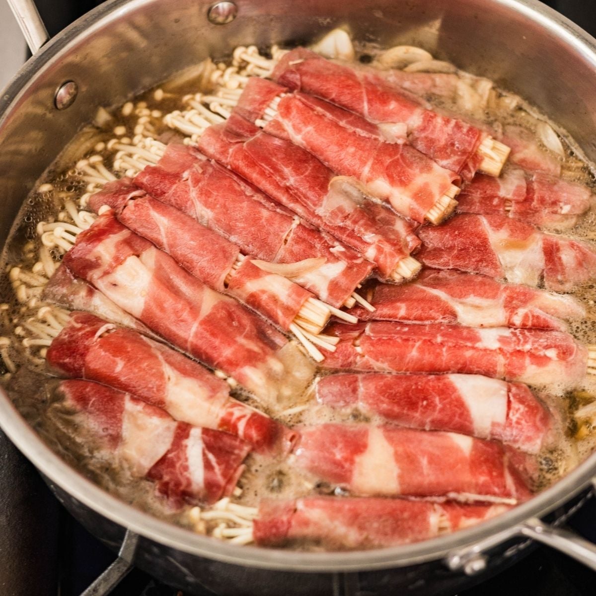 Enoki beef rolls simmering in dashi broth until the beef loses its pink color