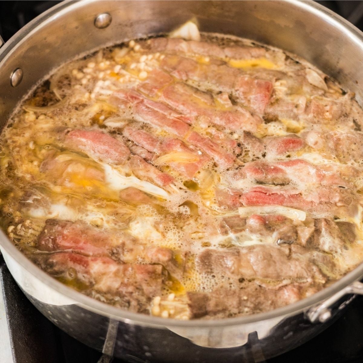 Beaten egg poured over enoki beef rolls in the pan