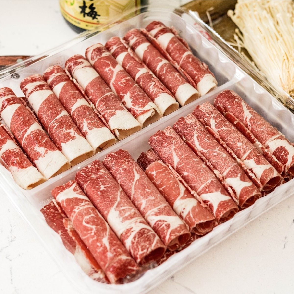 Frozen thinly sliced beef chuck rolls arranged on a sheet pan before filling