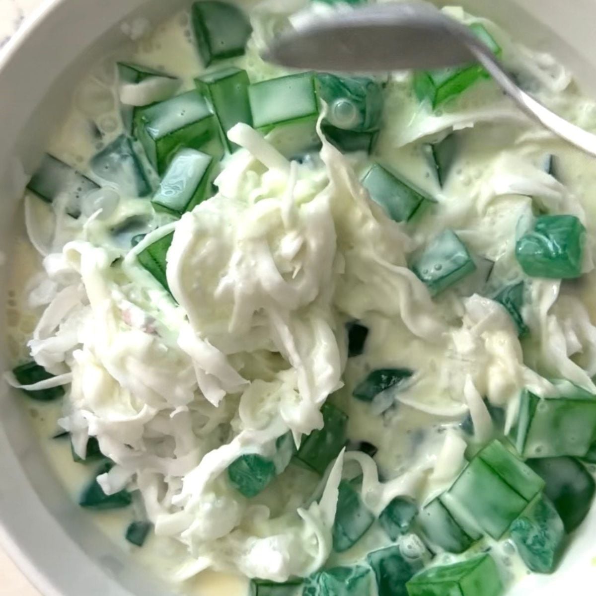 Buko pandan salad being mixed with coconut, pandan jelly, and creamy dressing