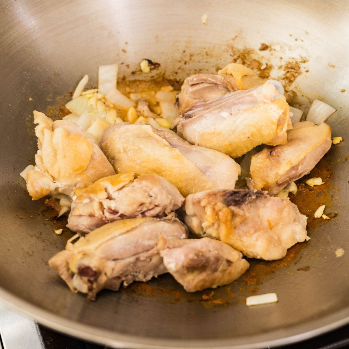 Chicken thighs browning with garlic and onion in a pan