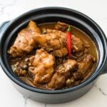 Chicken adobo sa gata simmering in a black pot with red chilies