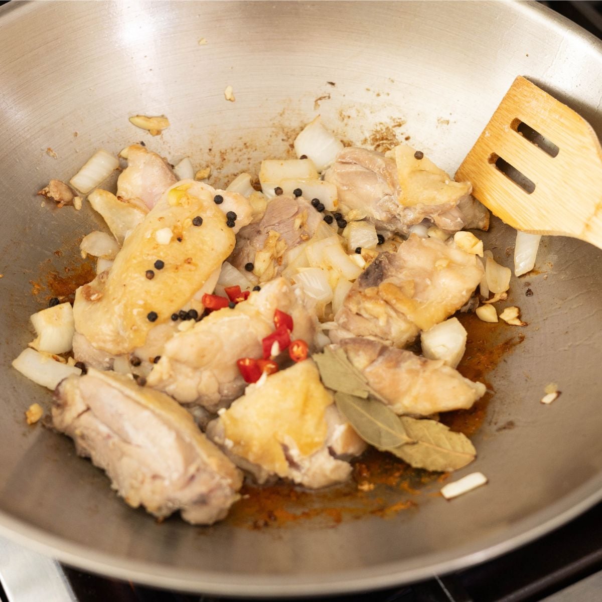 Whole peppercorns, bay leaves, and red chilies added to chicken in a pan