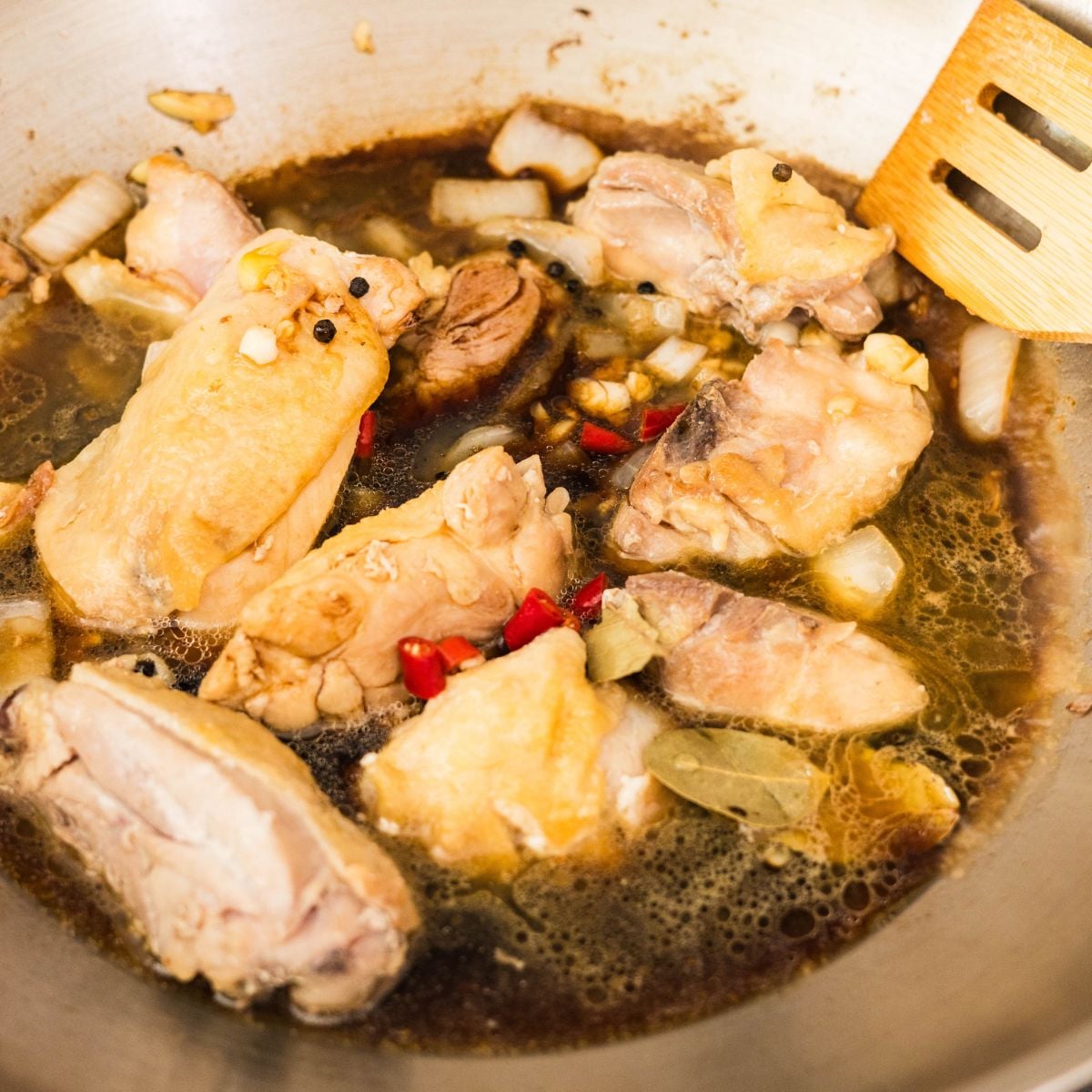 Soy sauce and vinegar poured over browned chicken thighs in a pan