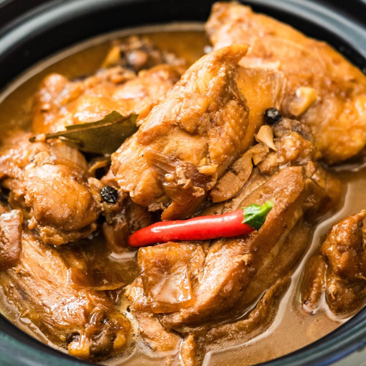 Chicken adobo sa gata in a black pot with red chilies and creamy coconut sauce