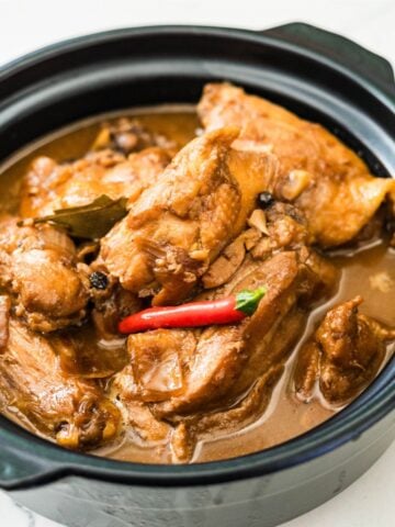 Chicken adobo sa gata in a black pot with red chilies and creamy coconut sauce