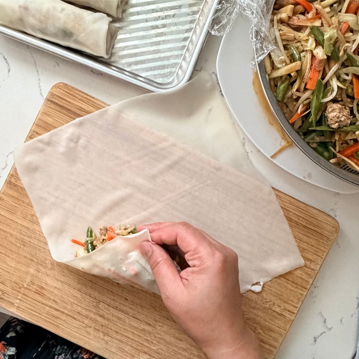 Folding the bottom corner of a wrapper to make lumpiang gulay
