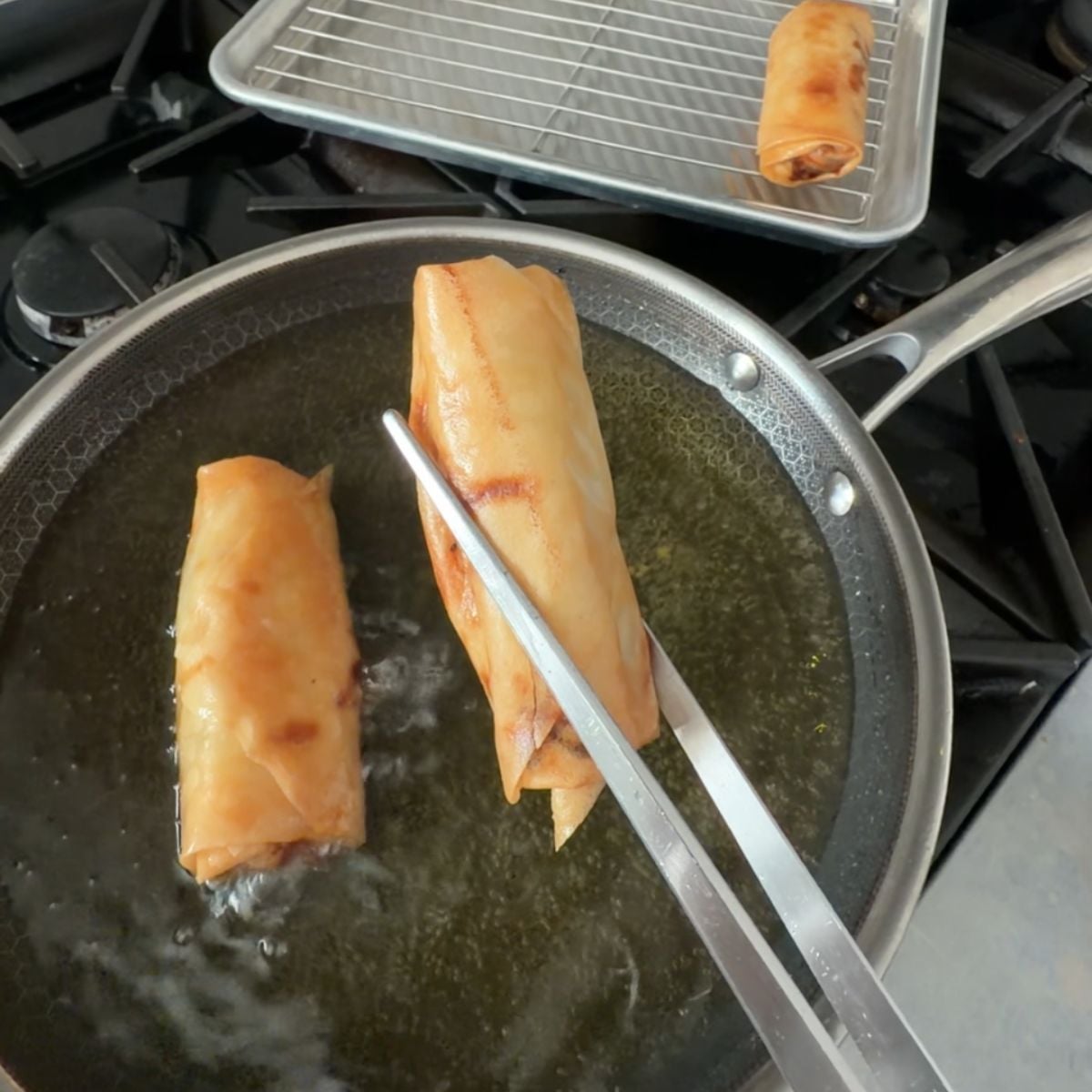 Turning lumpiang gulay while frying in hot oil