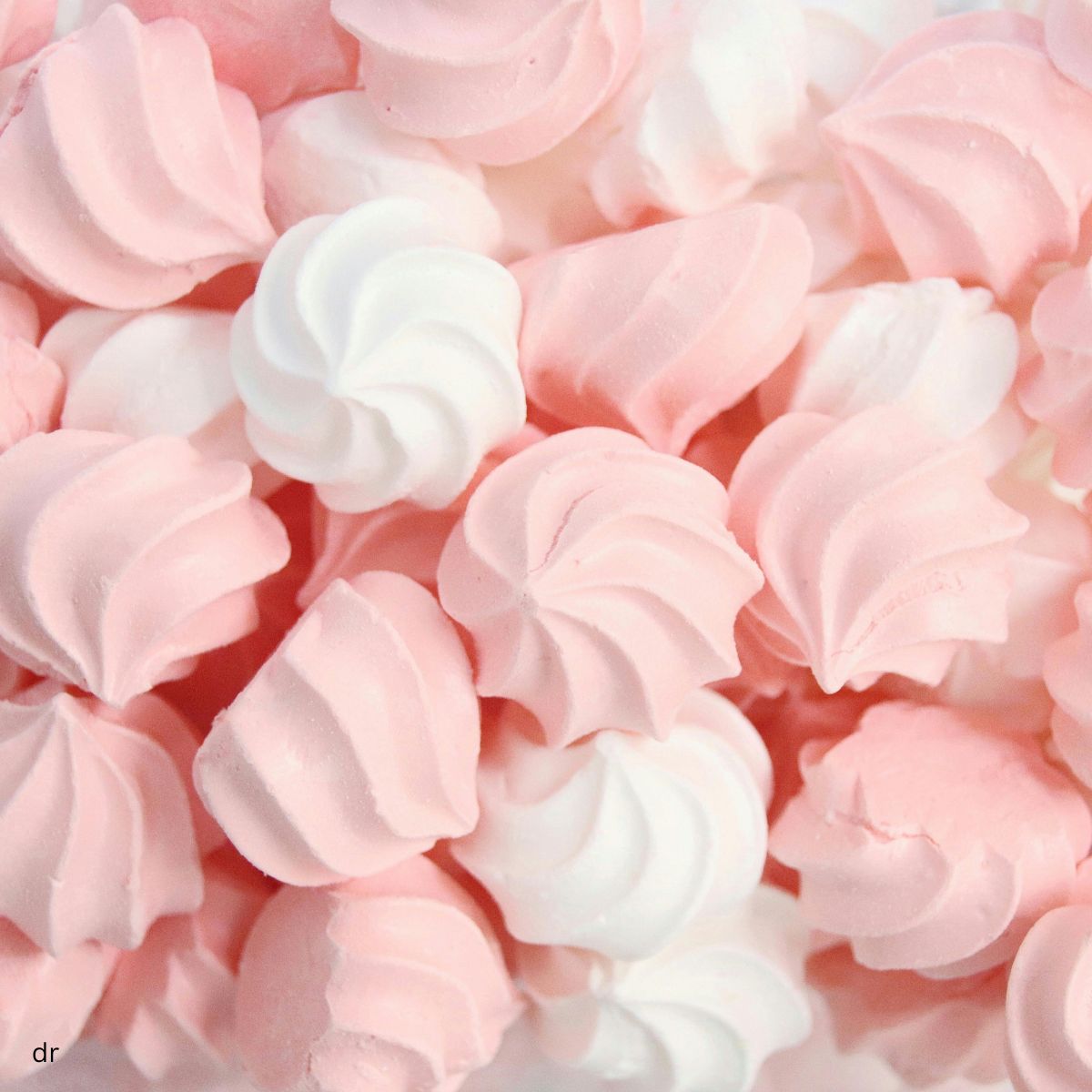 Close-up of piped pink and white meringue kisses piled together.