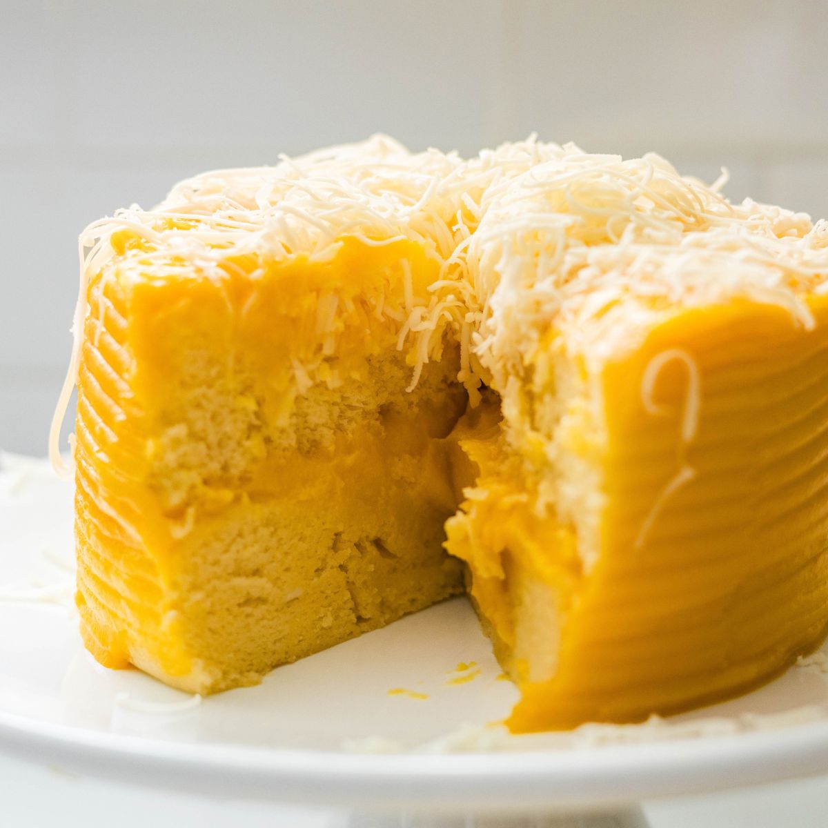 Yema cake with a slice cut out, showing the soft yellow crumb under the frosting and grated cheese.