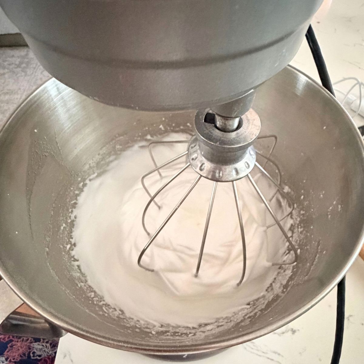 Egg whites whipped to soft, glossy peaks in a stand mixer bowl with the whisk attachment.