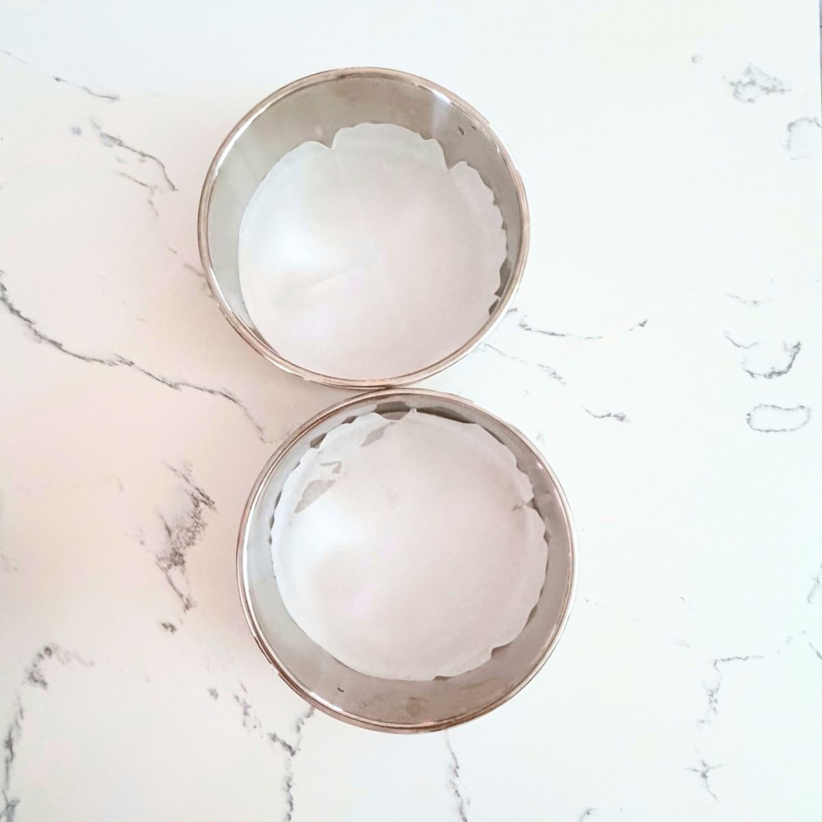 Two round cake pans lined with parchment paper on a marble counter.