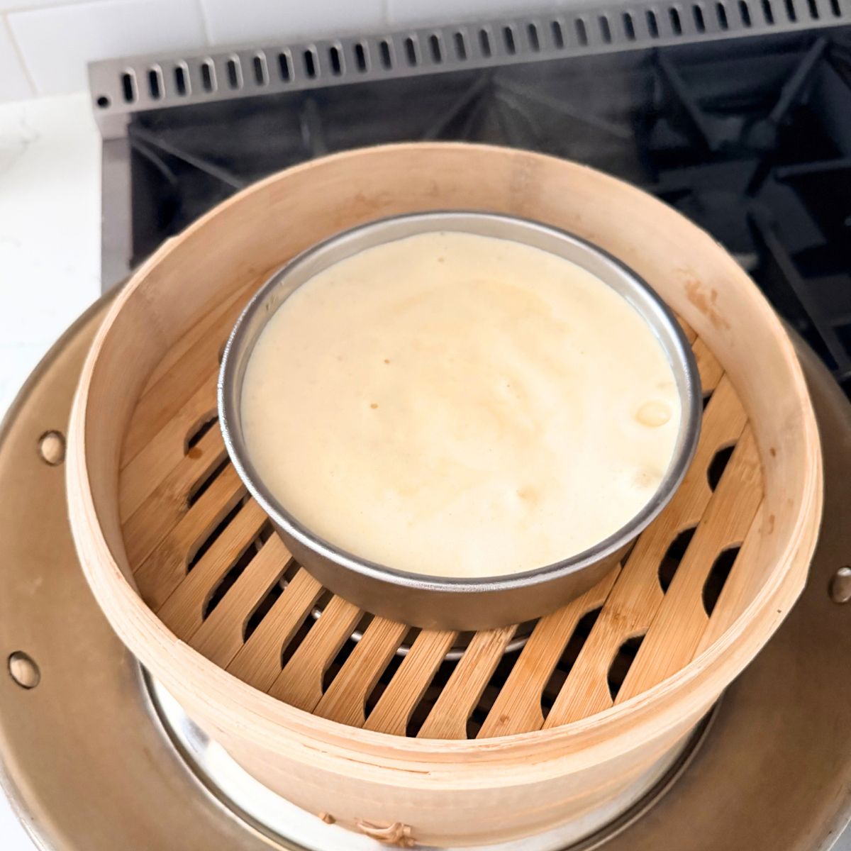 Pale yema cake batter in a round metal pan set inside a bamboo steamer.