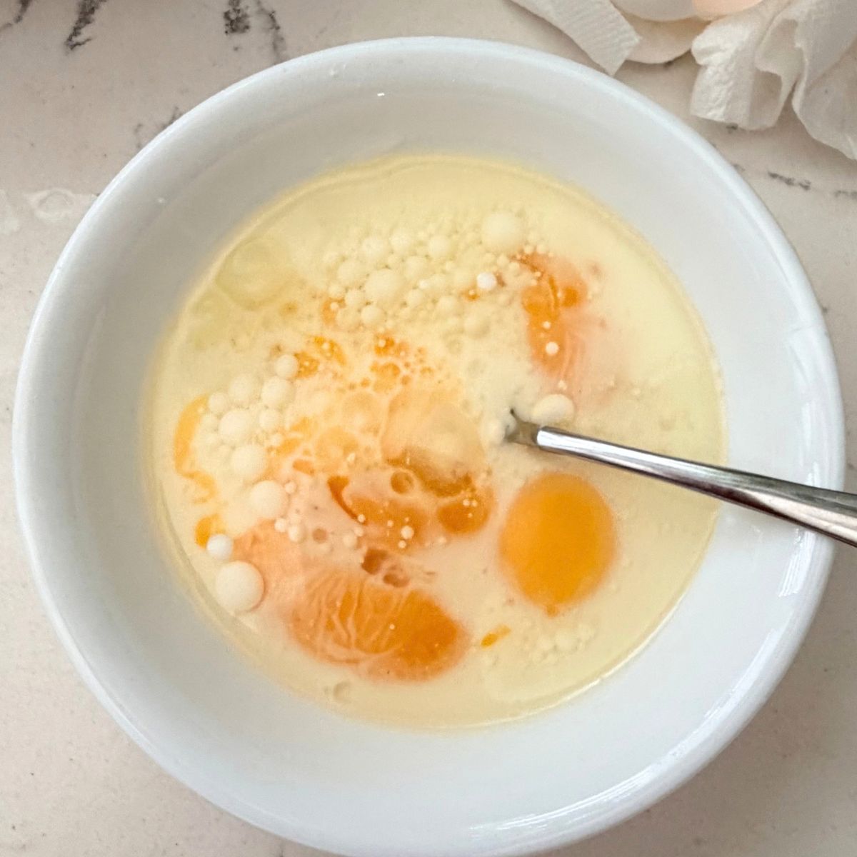 Egg yolks, milk, and oil in a glass mixing bowl with a whisk, ready to be combined for yema cake batter.