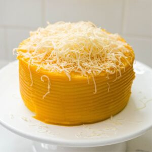 Yema cake covered in golden frosting and topped with a mound of finely grated cheese.