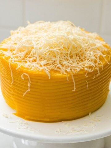 Yema cake covered in golden frosting and topped with a mound of finely grated cheese.