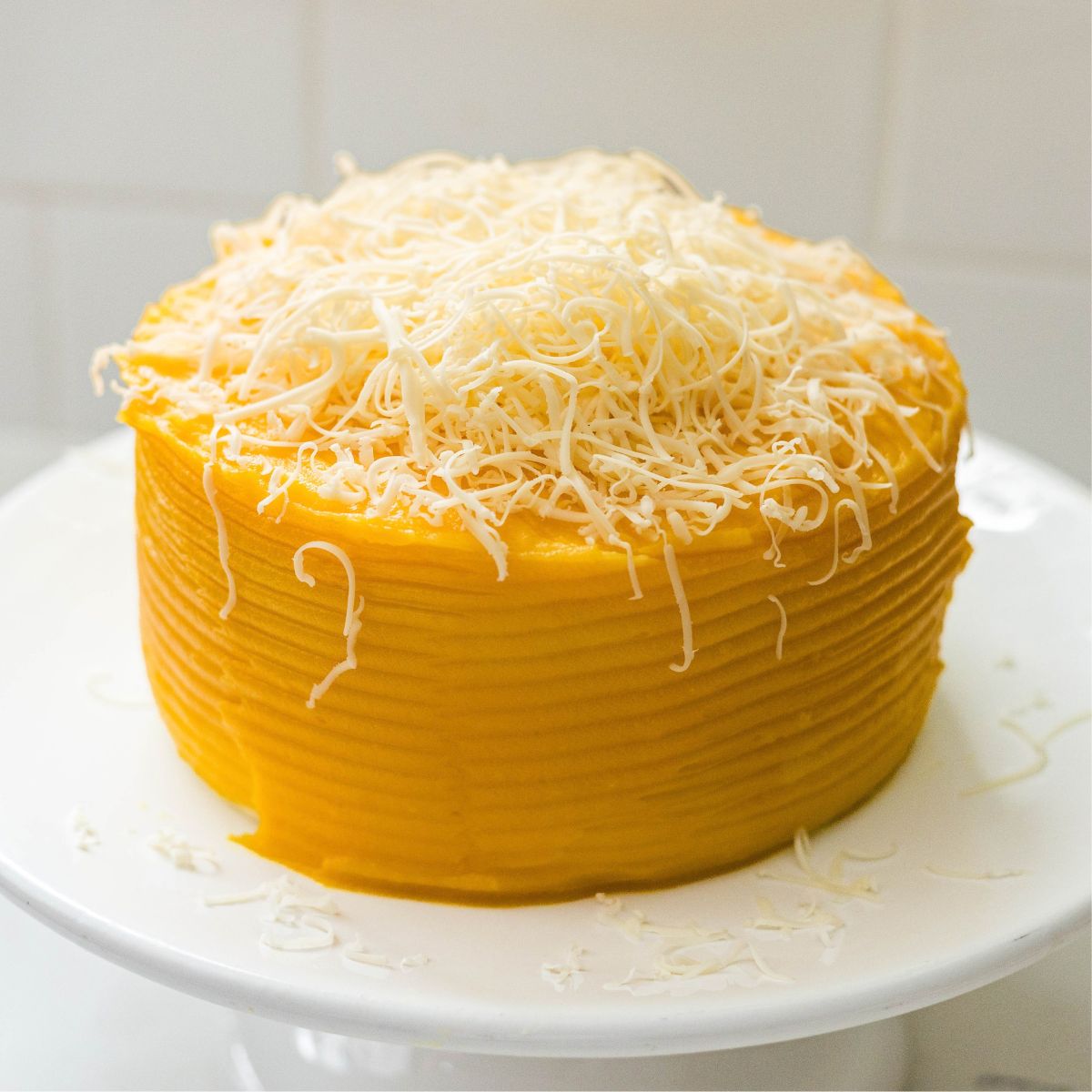 Yema cake covered in golden frosting and topped with a mound of finely grated cheese.