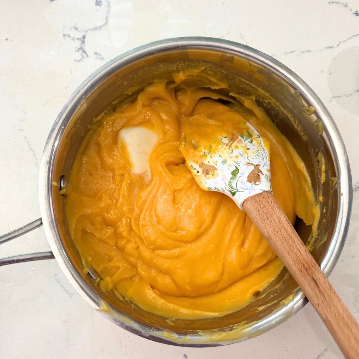 Thick orange yema frosting being stirred with a white spatula in a stainless steel saucepan.