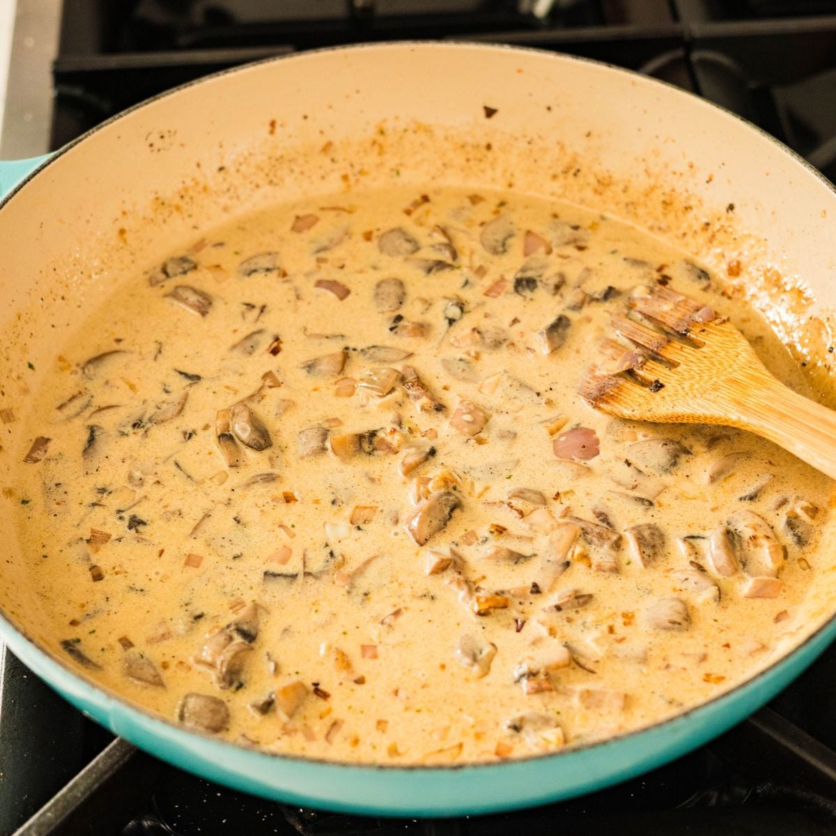 Evaporated milk simmering with mushrooms in a pan for Filipino carbonara