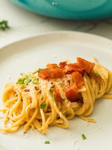 Filipino carbonara with crispy bacon and parsley on a white plate.