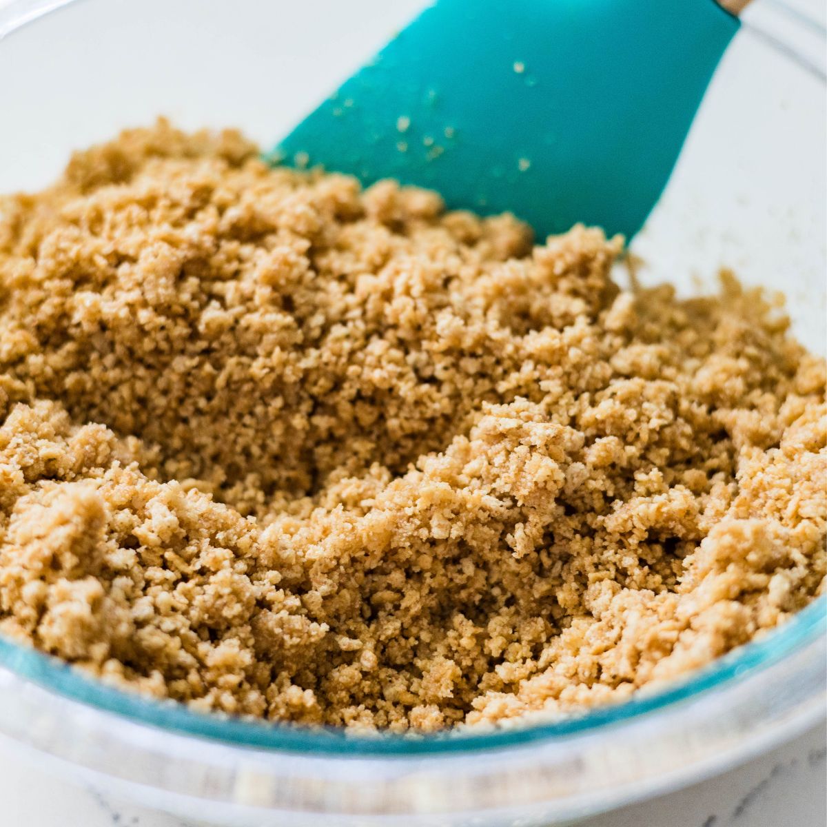 Graham cracker crumbs mixed with melted butter in a glass bowl with a spatula