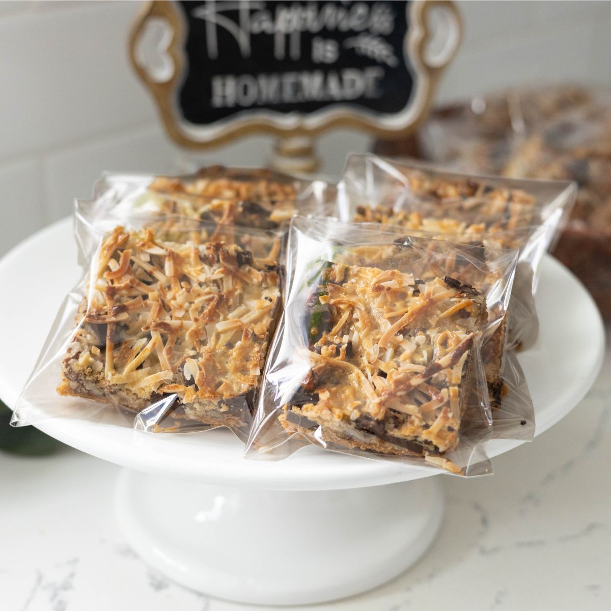 Individually wrapped homemade magic cookie bars stacked on a white cake stand