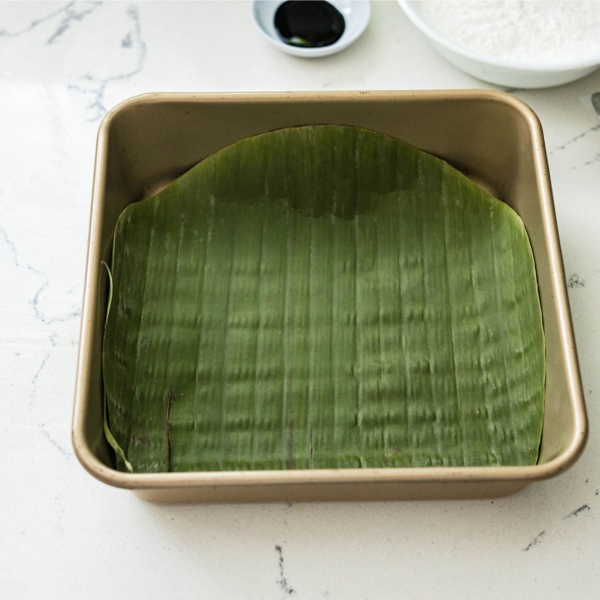 Square baking pan lined with banana leaves for making inutak