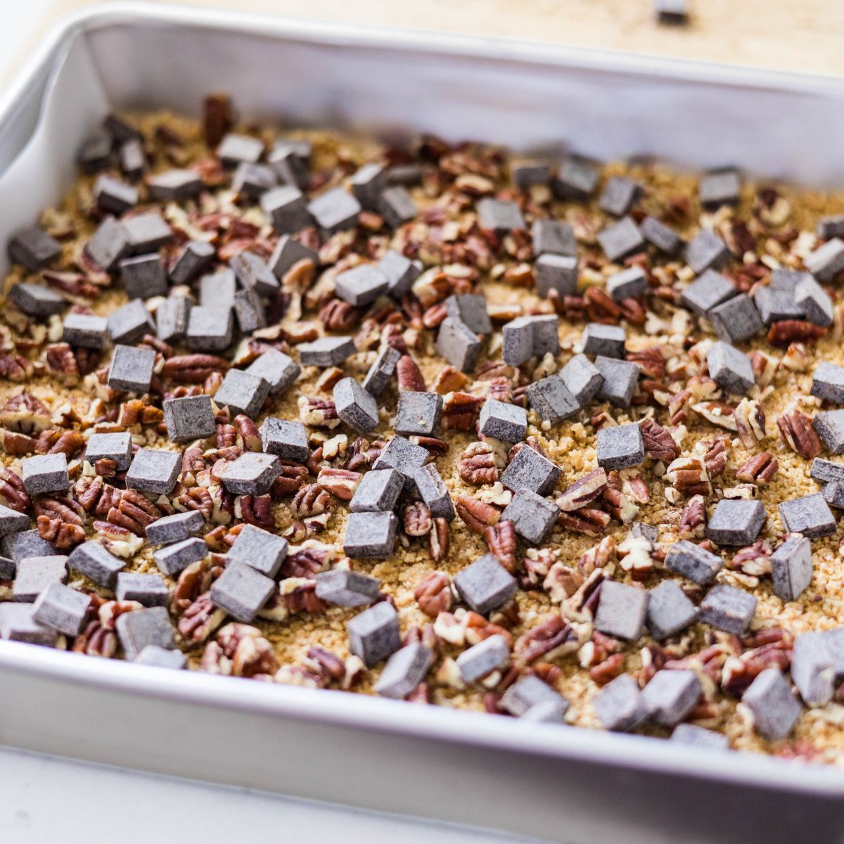 Chocolate chips and chopped pecans scattered over a graham cracker crust in a baking pan