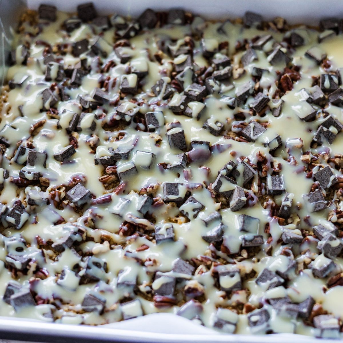 Sweetened condensed milk drizzled over chocolate chips and pecans on a graham cracker crust