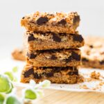 Stack of magic cookie bars showing the graham cracker crust, chocolate chips, pecans, and toasted coconut layers