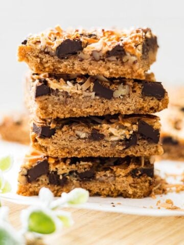 Stack of magic cookie bars showing the graham cracker crust, chocolate chips, pecans, and toasted coconut layers